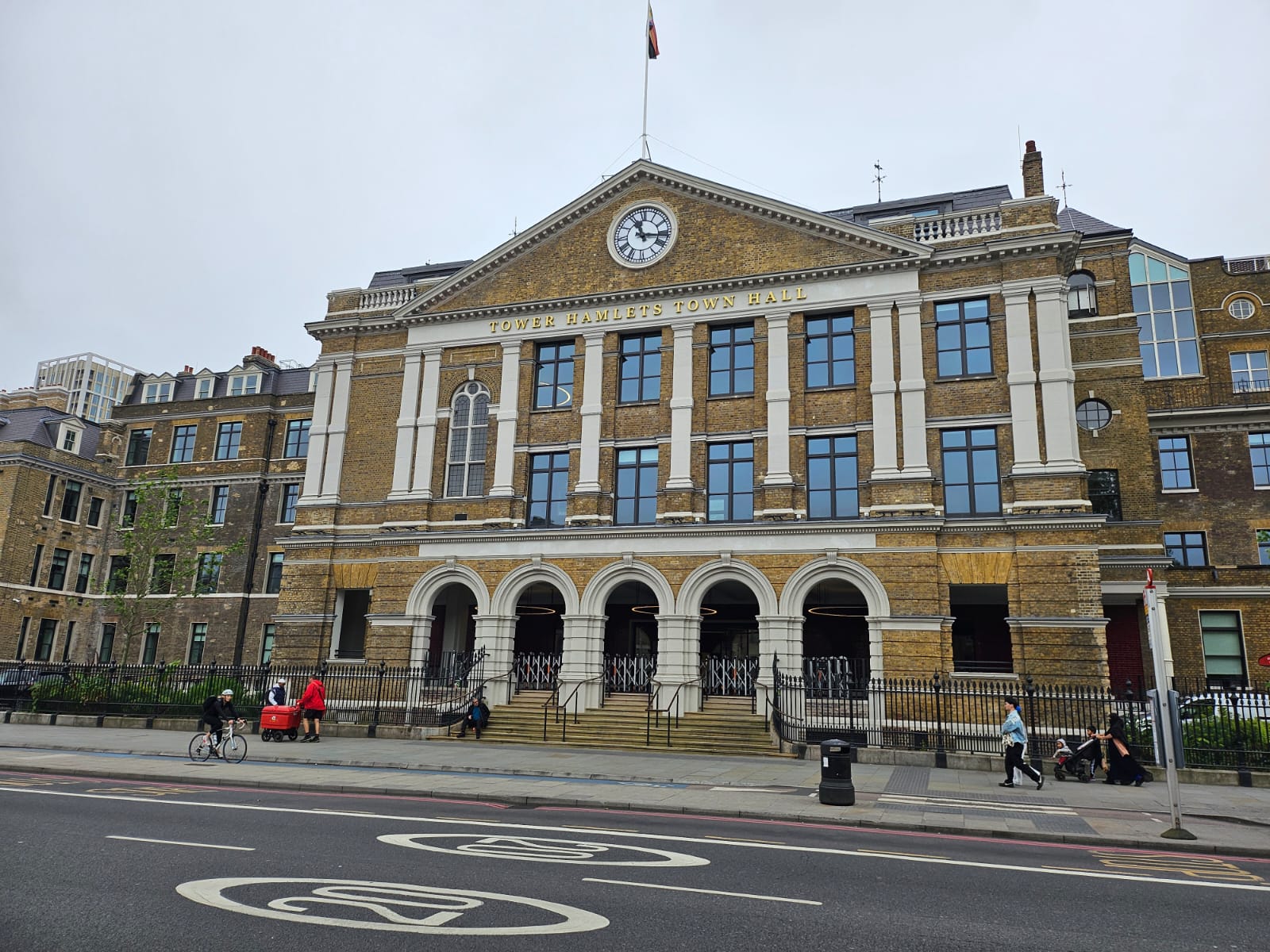 A large, light coloured brick building with an arched portico up a flight of steps. Above it are two floors of tall windows, topped with a pediment. There's a clock in the centre of the pediment and a flag pole on the top. The building used by the London Hospital, but is now Tower Hamlets Town Hall and this is written across the front of the building.