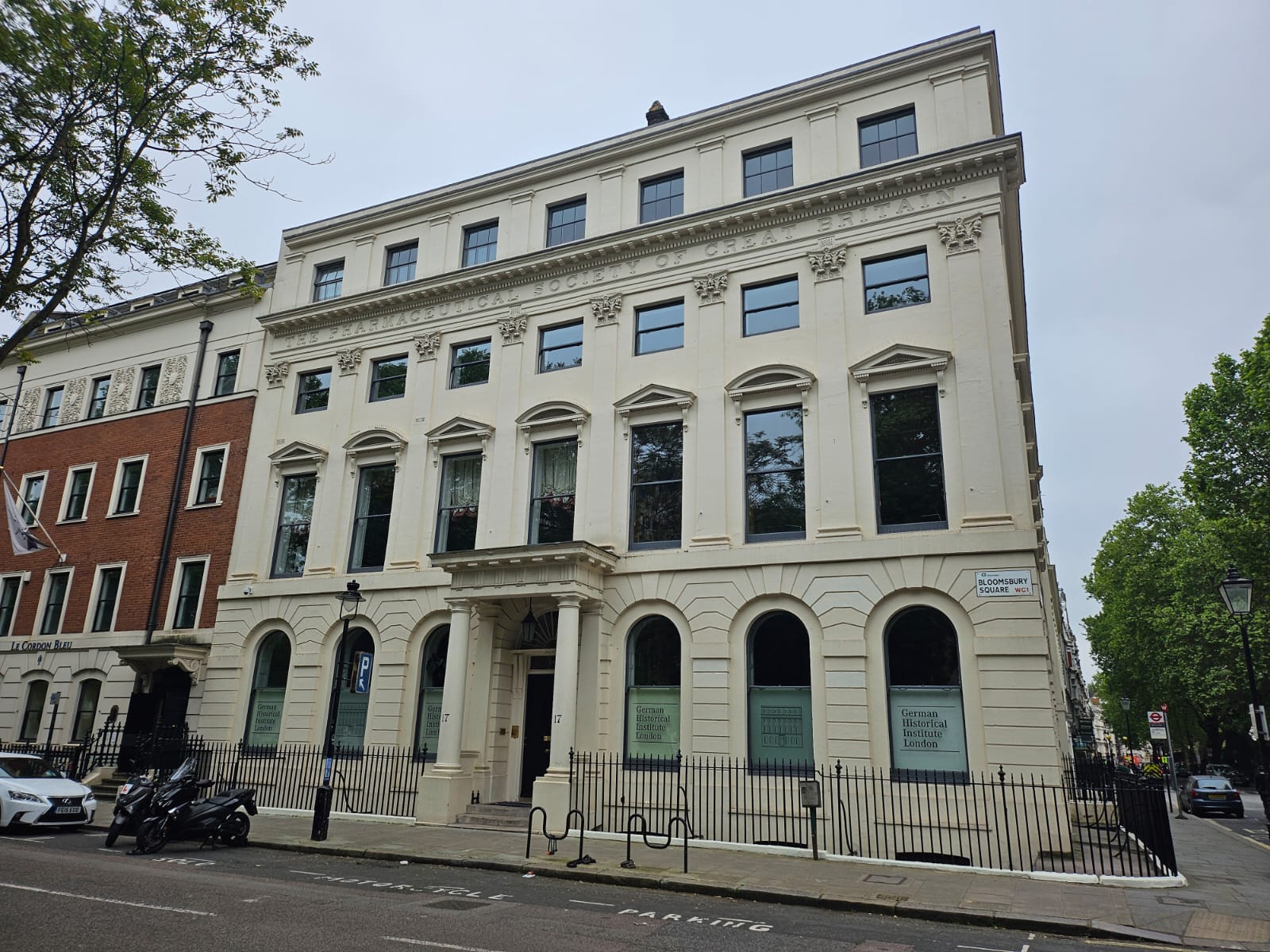 The former building of the Royal Pharmaceutical Society on Bloomsbury Square. A classical, regency building. White. Four stories tall with a symetrical frontage and a central pillared entrance. Surrounded by railings.